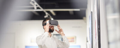 Side view portrait of modern bearded man wearing VR gear while enjoying immersive experience during exhibition in art gallery, copy space